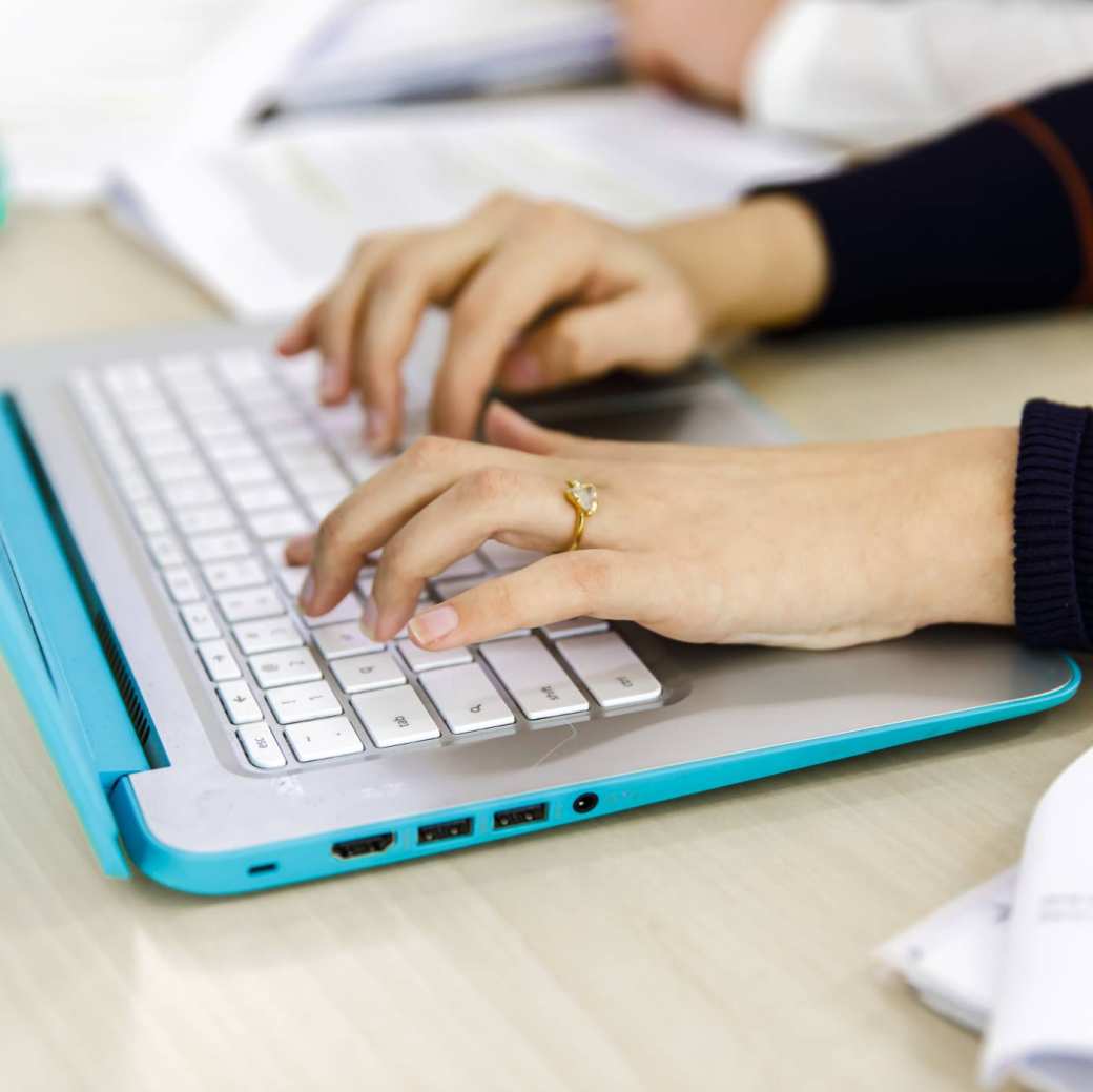 Twee vrouwenhanden typen op het toetsenbord van haar laptop.