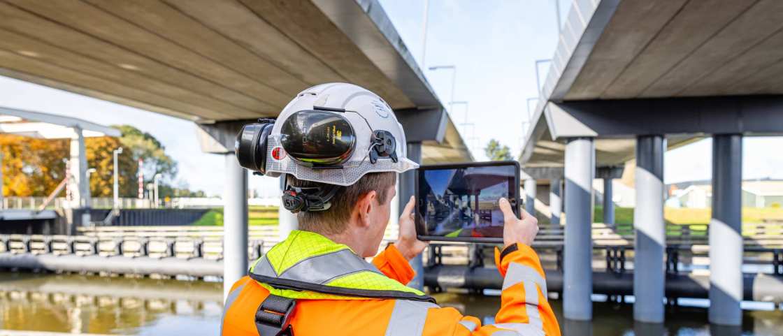 projectleider fotografeert met een tablet het werk aan een viaduct
