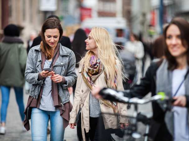 vrouwen lopend door de stad, eentje met fiets, eentje met mobiel