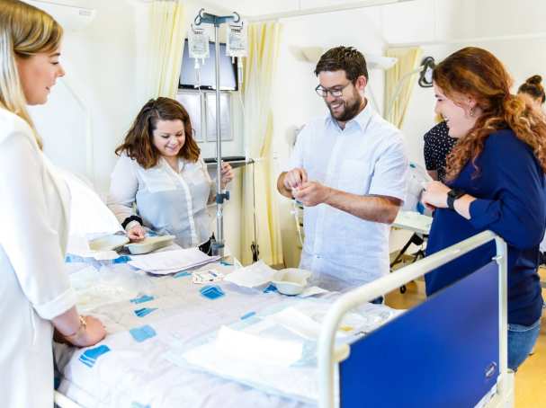 docent lachend met studenten om ziekenhuisbed