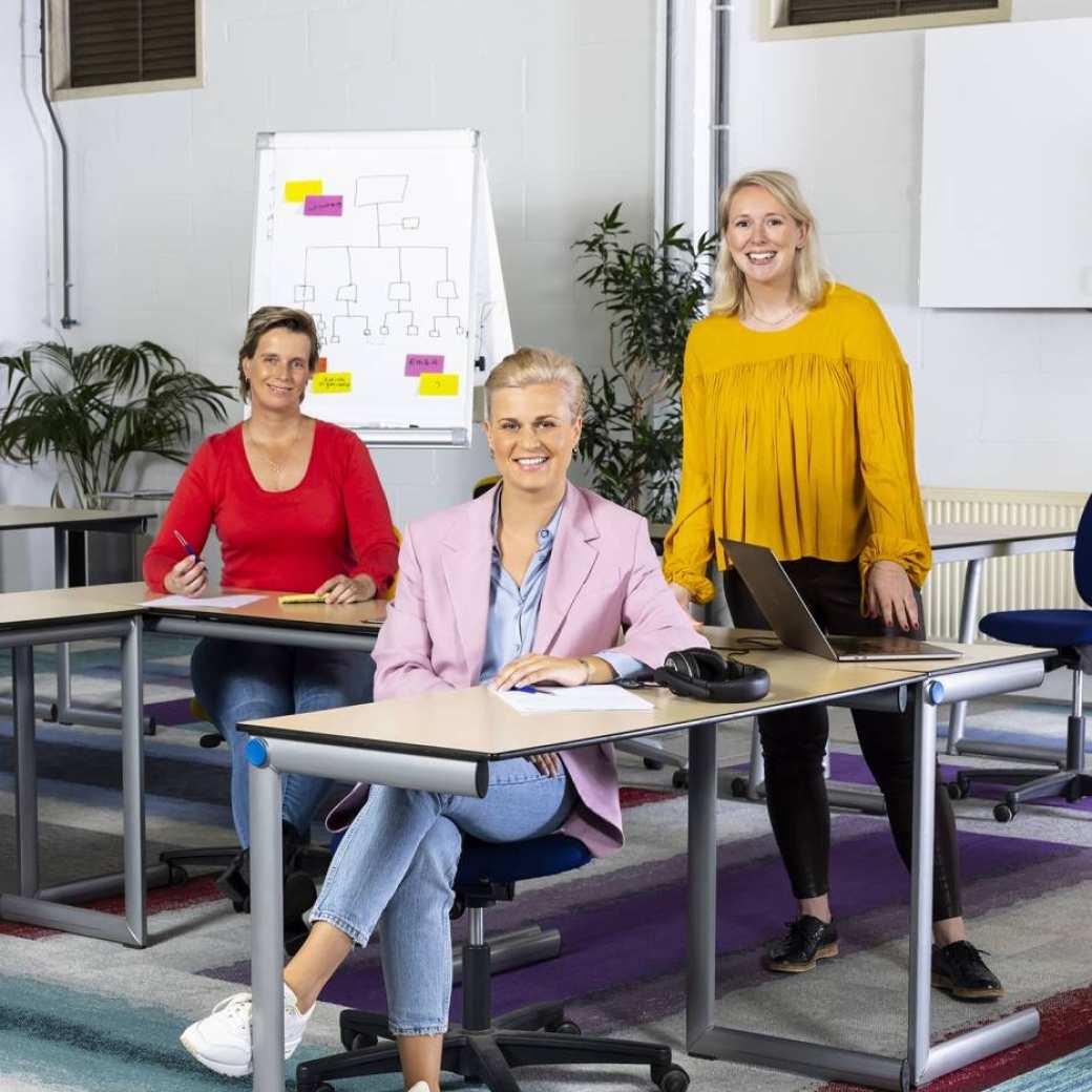 Drie personen achter een tafel in een klaslokaal op de campus op de opleiding associate degree logistiek deeltijd