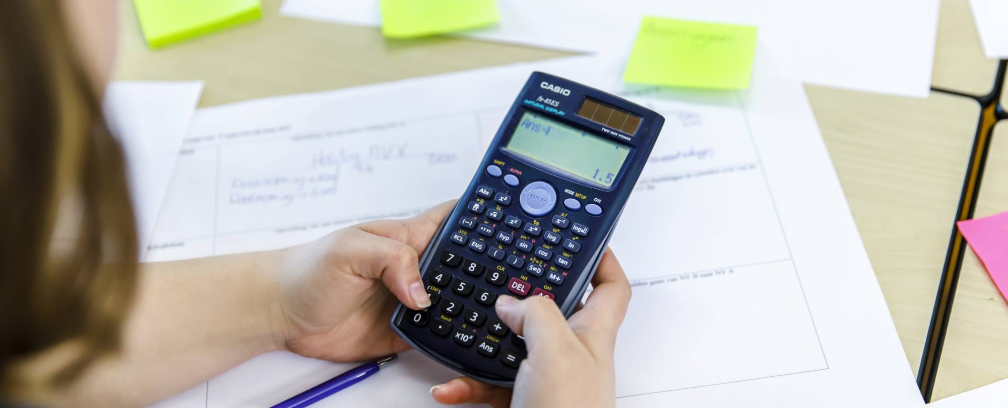 Close-upfoto van student die een som intypt op de rekenmachine.