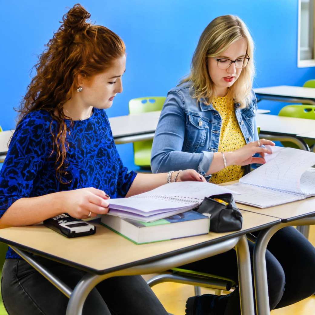 Twee wiskunde studenten bladeren door het lesboek, terwijl ze in het klaslokaal zitten.
