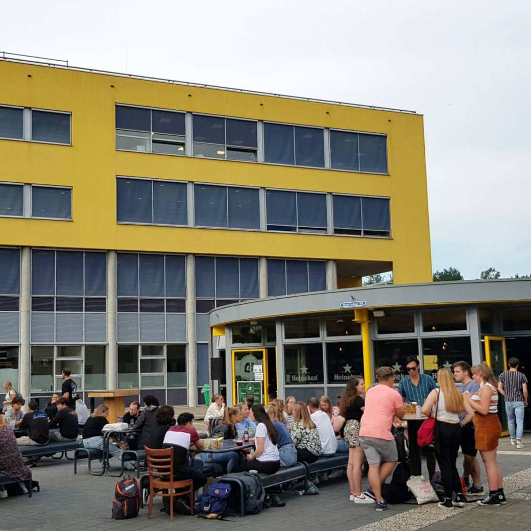 321306 Studenten komen na de lessen samen bij Lokaal 99 om iets te drinken. Op de achtergrond het onderwijsgebouw van Engineering en Automotive.