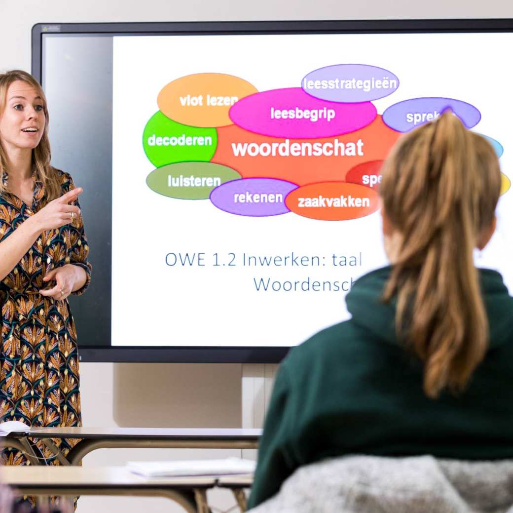 ALPO leraar heeft een PowerPoint openstaan met 'Woordenschat' erop en geeft een student de beurt.