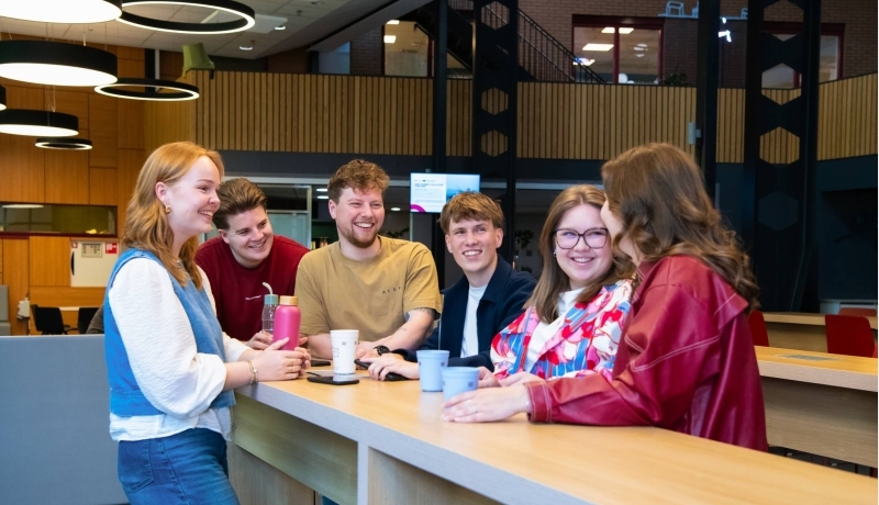 Studenten praten met elkaar aan de uitleenbalie van Ergotherapie met koffie en thee.