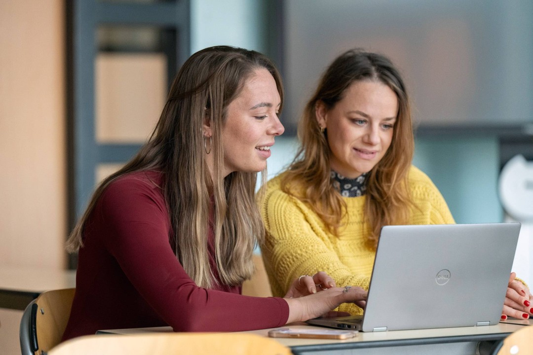 2 studenten kijken lachend samen naar een laptop.