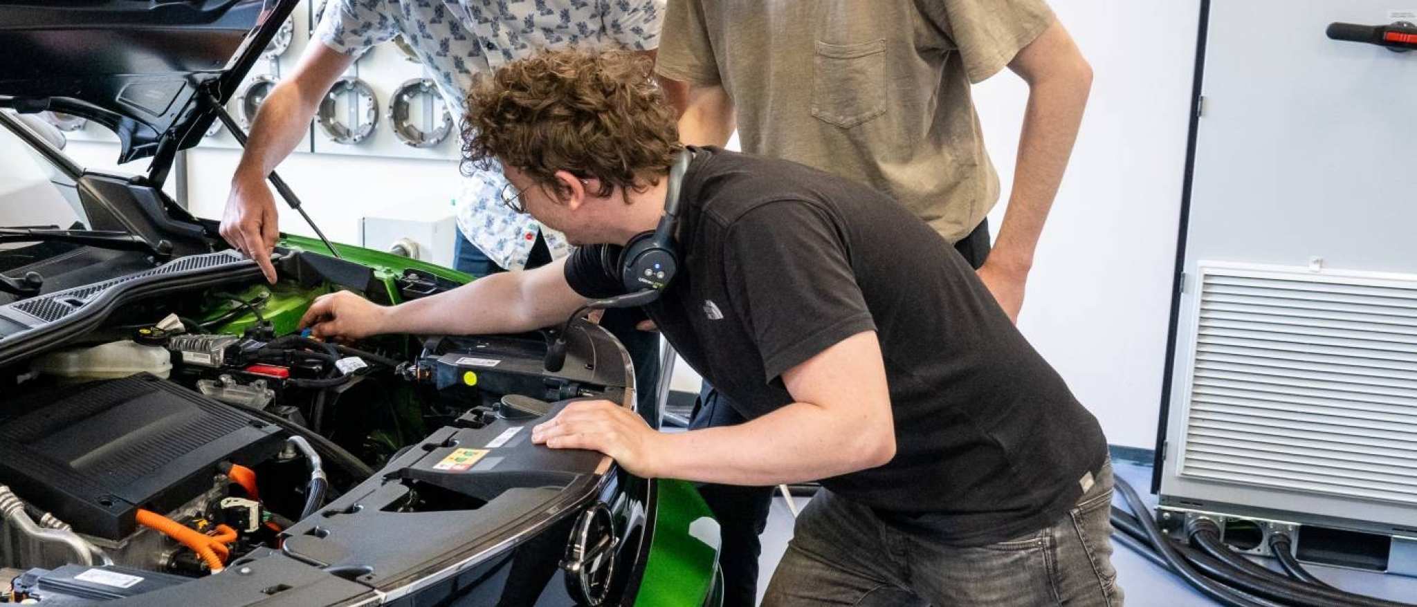 Studenten en docent automotive kijken naar de motor van de auto.