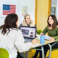 Docent geeft les aan haar drie studenten in een lokaal met de Engelse vlag aan de muur.