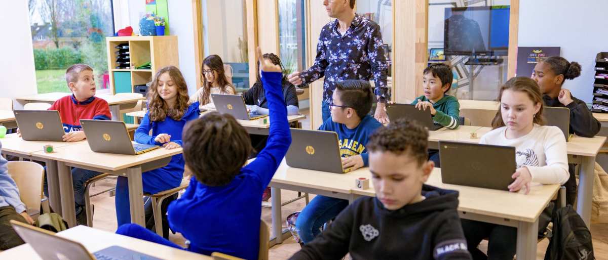 Groep 5,6,7 op de school Da Vince. Een jongen steekt zijn vinger op in de klas. 