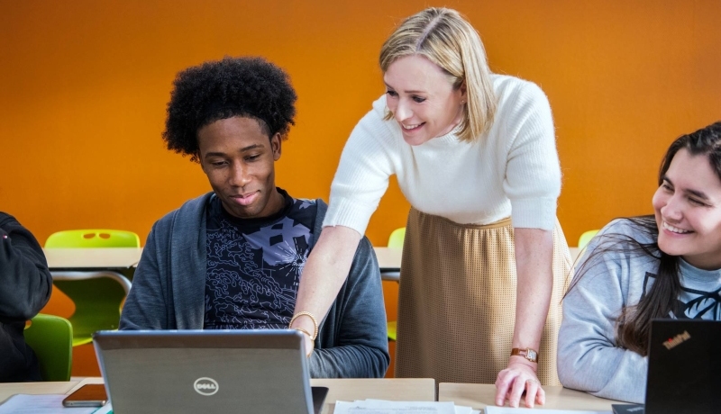docent wijst lachend op laptop bij twee masterstudenten