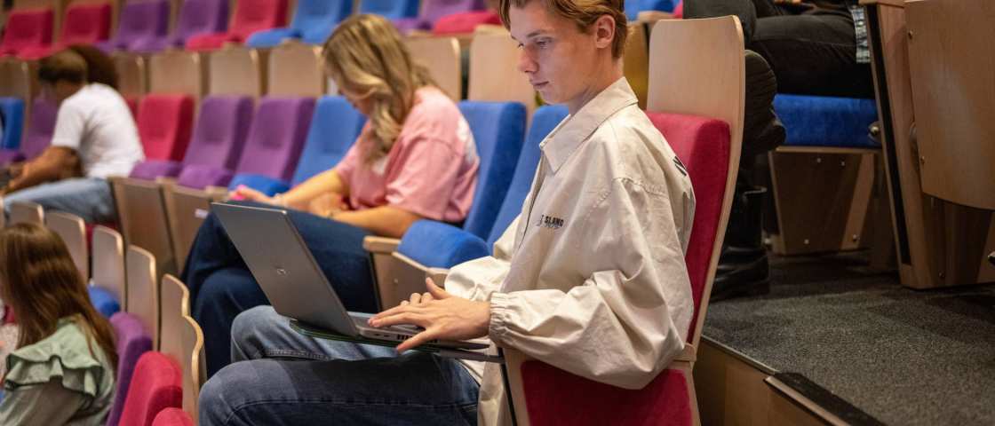 Jongen en meisje in collegezaal werken op laptop en noteren aantekeningen. 
