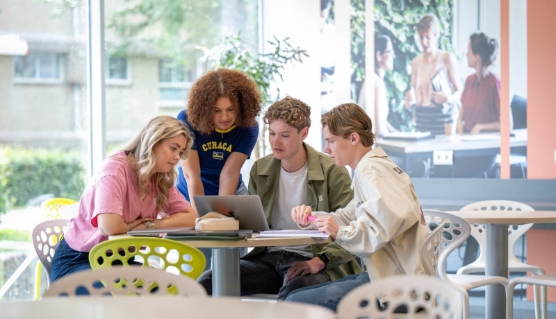 Groepje studenten werken samen aan een ronde tafel in de gang, werkplek in LvS10. Kijken samen naar de laptop.