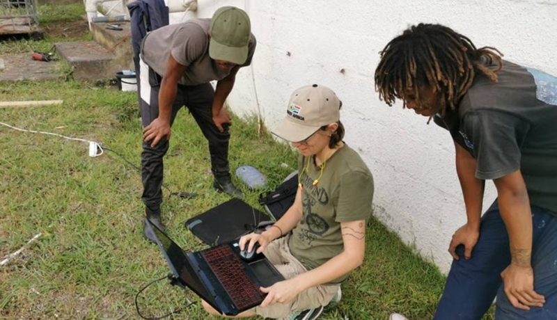 Student Industrieel Product Ontwerpen Esmeralda laat haar werk zien op een laptop op een grasveld in Zuid-Afrika aan samenwerkingspartners.