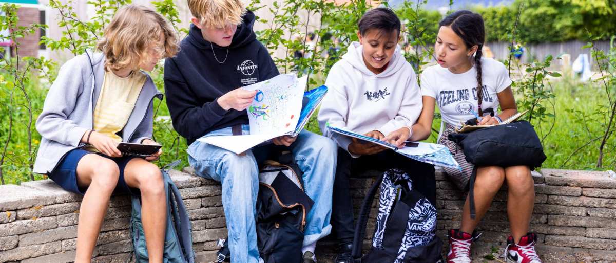 Vier leerlingen lezen buiten op een bankje. Foto van de opleiding leraar basisonderwijs