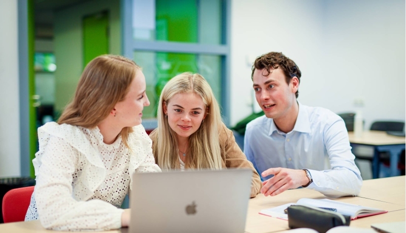 Twee studenten en een docent in overleg achter een laptop
