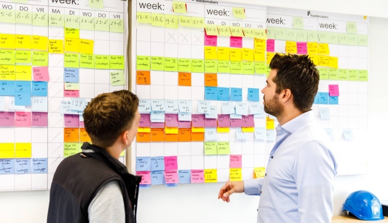 Twee medewerkers van het lectoraat Wijkverpleging van de HAN kijken op een planningsbord.