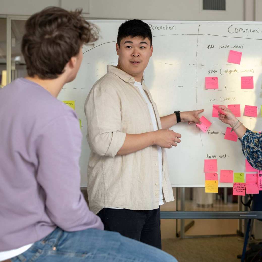 Drie studenten plakken post-its en overleggen samen, projectonderwijs in de klas.