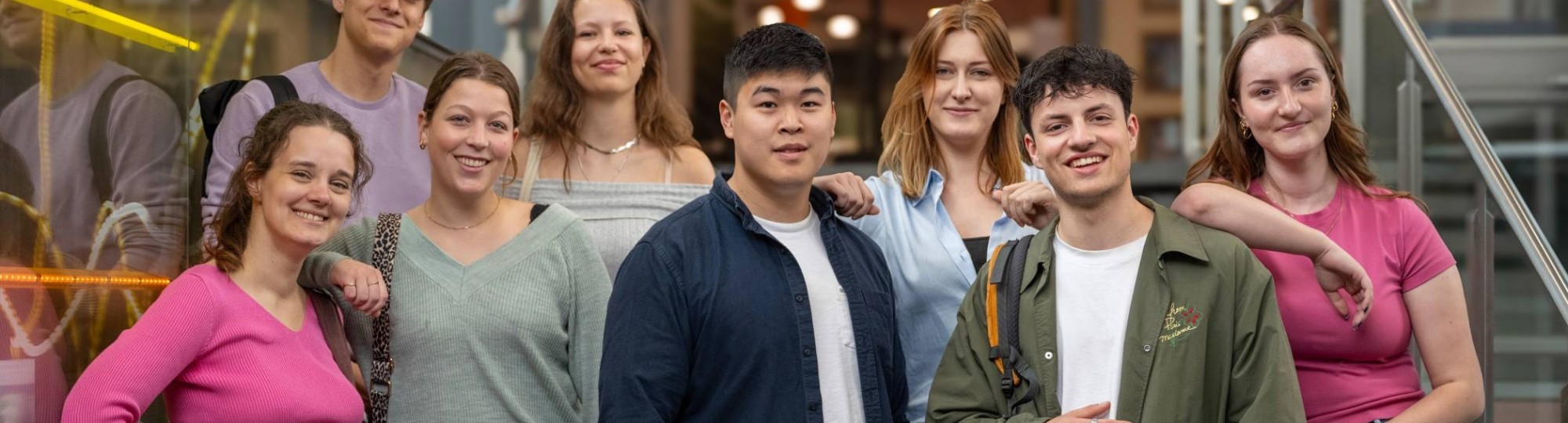 Groep studenten lachen in de camera, staan in de lichtstraat van gebouw R26.