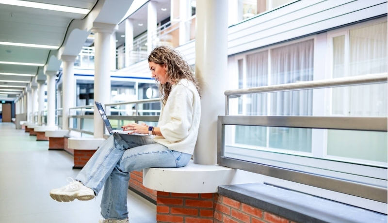 Duaal student Commerciële Economie werkt in gang op laptop.