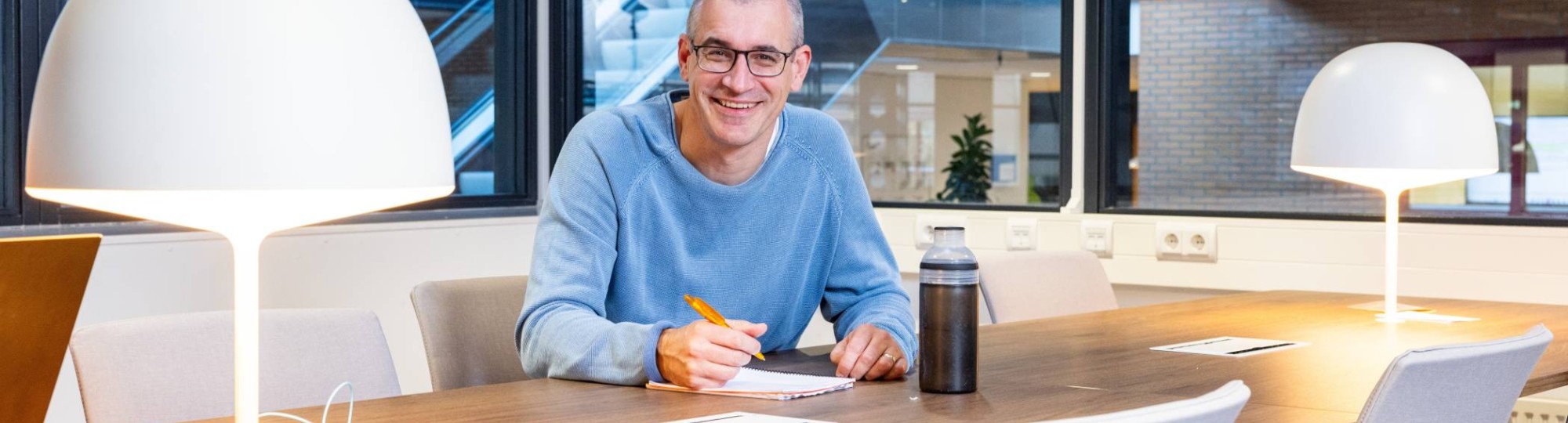 Guus Witjes zit aan een tafel en schrijft