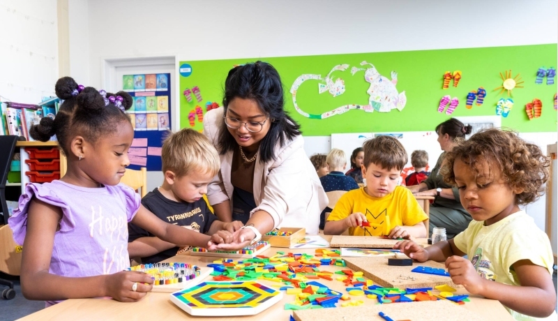 De kinderen in de klas leggen een puzzel en de lerares van de opleiding leraar basisonderwijs helpt hen hierbij.