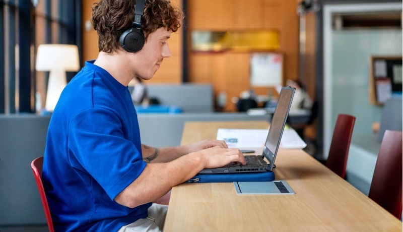 Student met koptelefoon werkt achter computer.