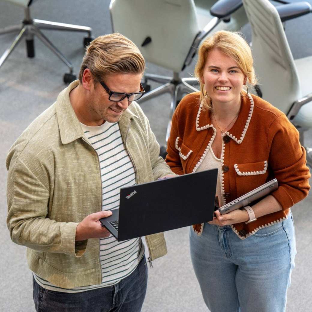 Man en vrouw staan met laptop in de hand en kijken lachend naar camera