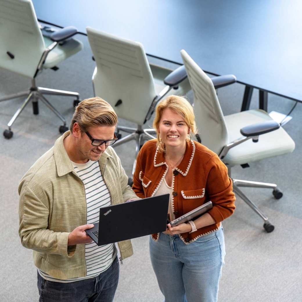 Man en vrouw staan met laptop in hand en kijken lachend naar camera