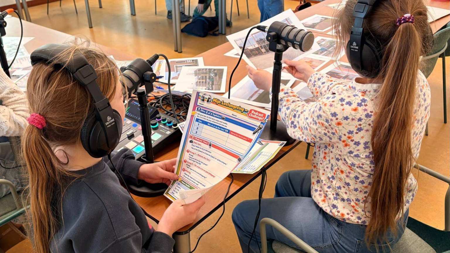 Foto van twee meisjes (met koptelefoons en foto's uit hun buurt) in gesprek met professionals over hun leefomgeving