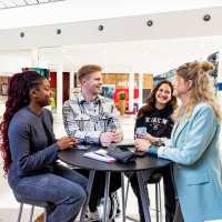 Leerlingen praten met elkaar om een tafel.