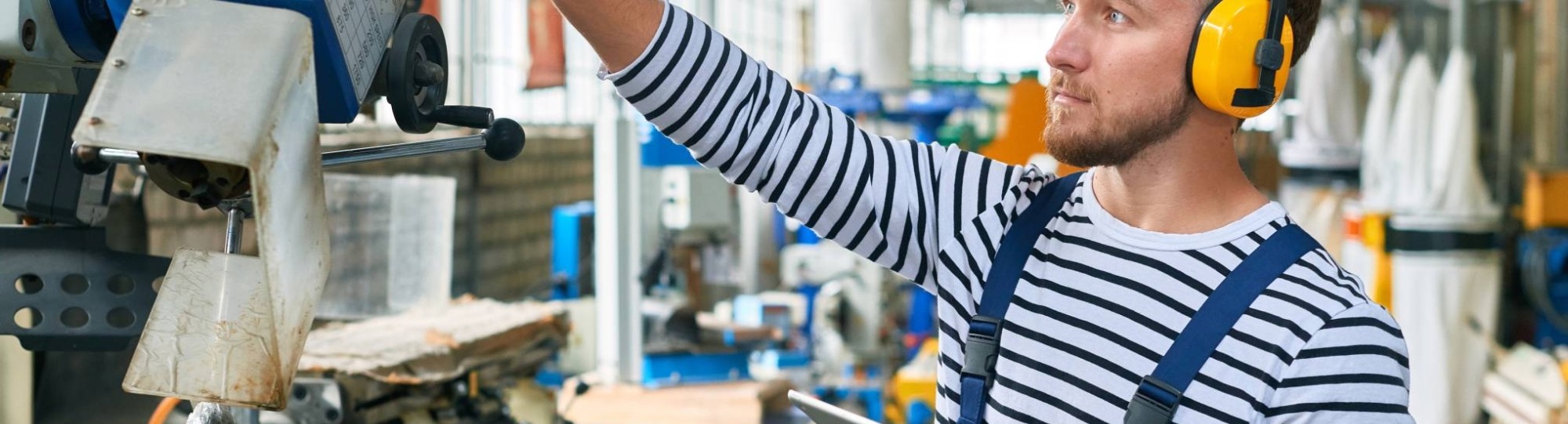 Jonge operator met gele gehoorbeschermers op de werkvloer van een moderne fabriek