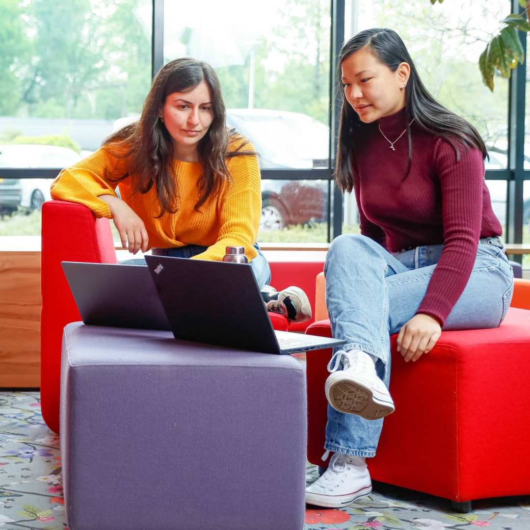 Twee internationael studenten overleggen met laptop bij rode banken