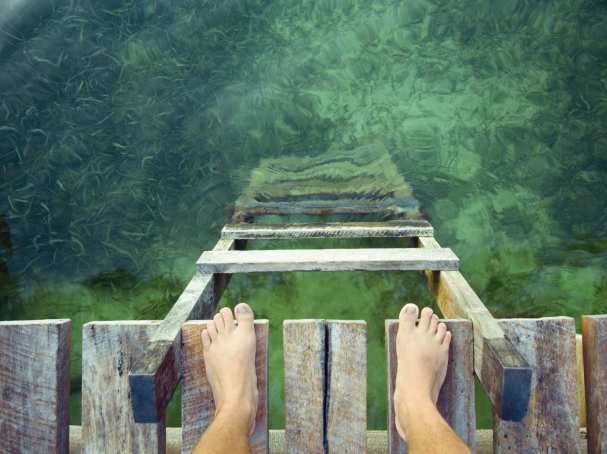 stockfoto van voeten op een vlonder aan de rand van groen water