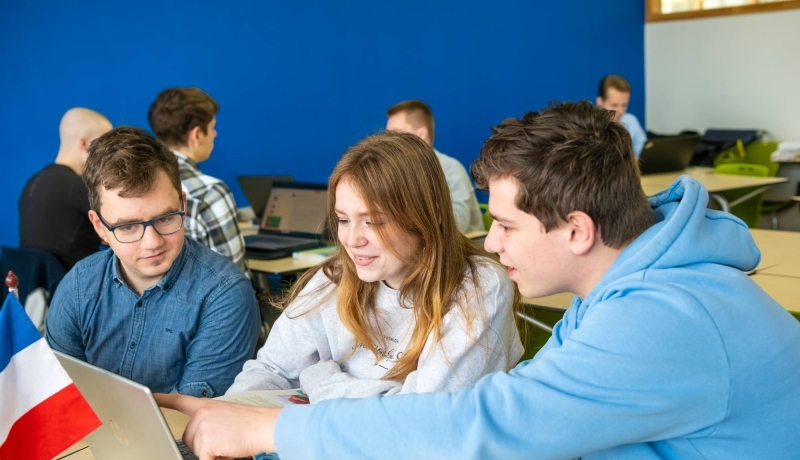 3 studenten Leraar Frans werken in de les met een Frans vlaggetje op tafel.