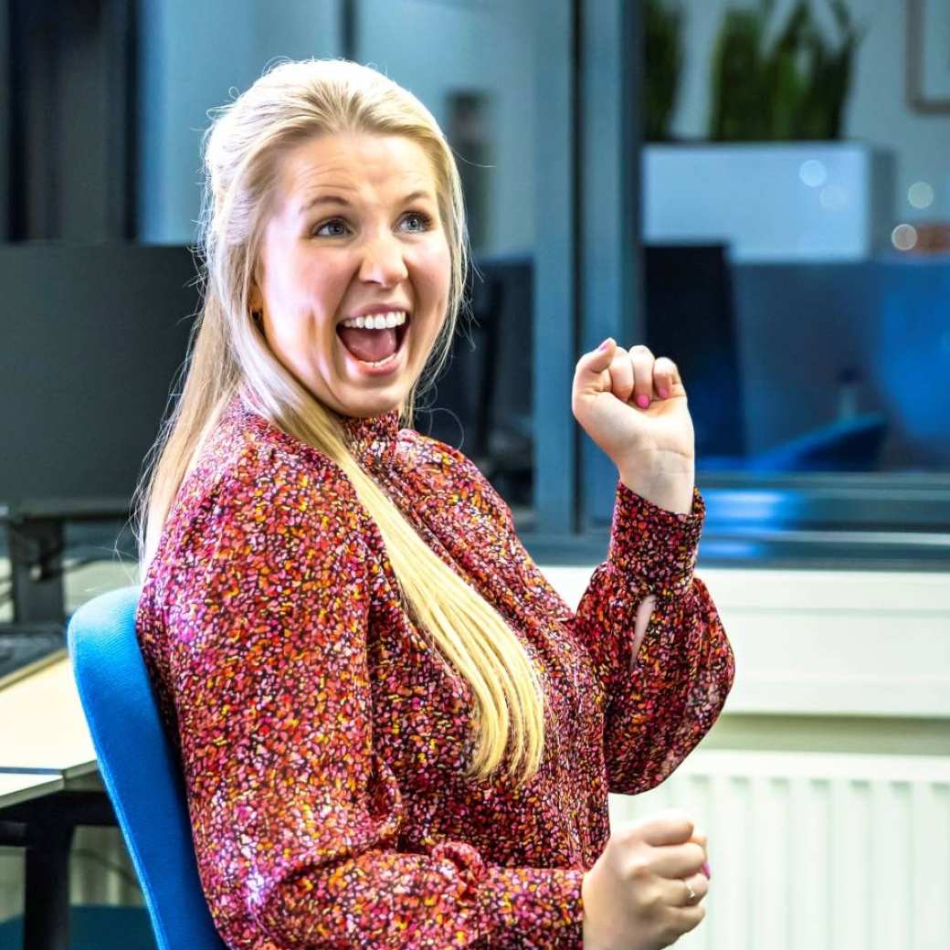 Vrouw draait lachend een rondje met haar bureaustoel en heeft haar hand in de lucht.