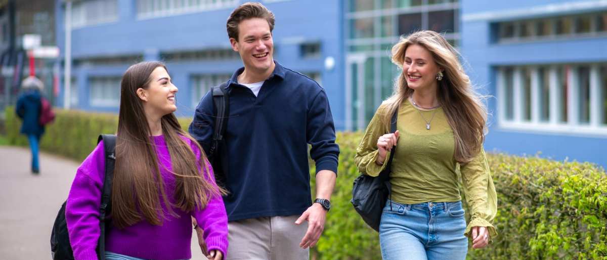 Drie studenten van Learning and Development in Organisations voltijd lopen lachend voor het HAN gebouw in Nijmegen.