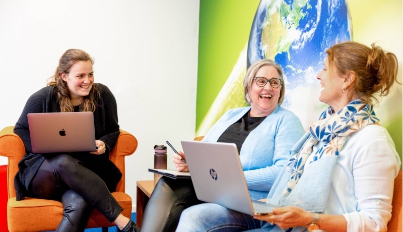 Drie vrouwen zijn aan het overleggen en hebben een laptop op hun schoot