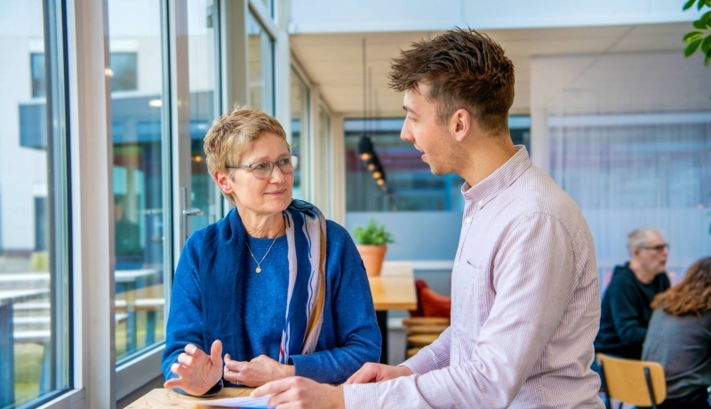Man en vrouw staan aan een tafel bij een raam te praten.