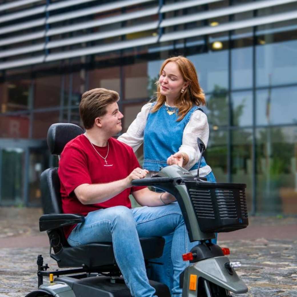 Jongen zit in scootmobiel kijkt naar student Ergotherapie buiten voor Kapittelweg 33 in Nijmegen