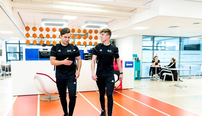 Twee jongens lopen in hun alo-tenue door de gang.