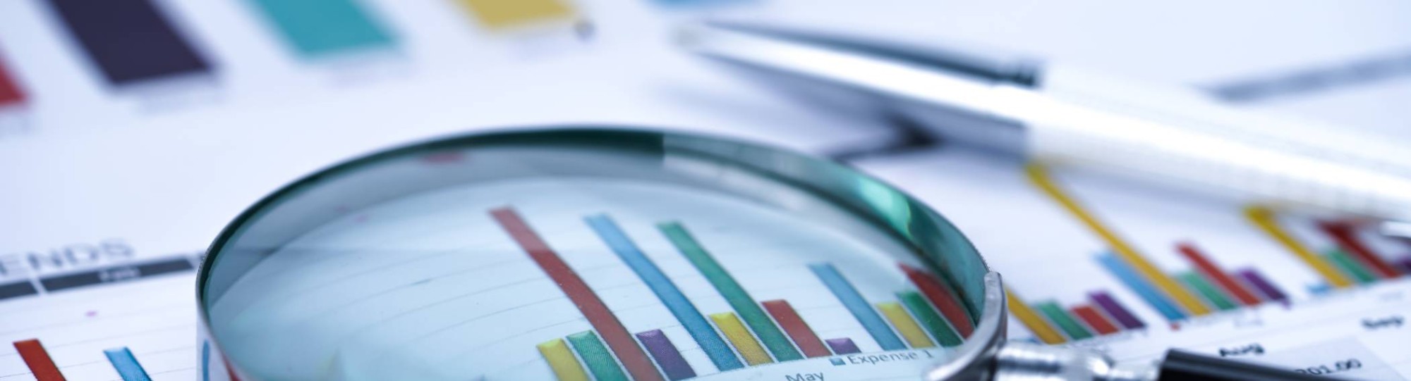 Close-up van een vergrootglas boven grafieken. Vaag een pen.