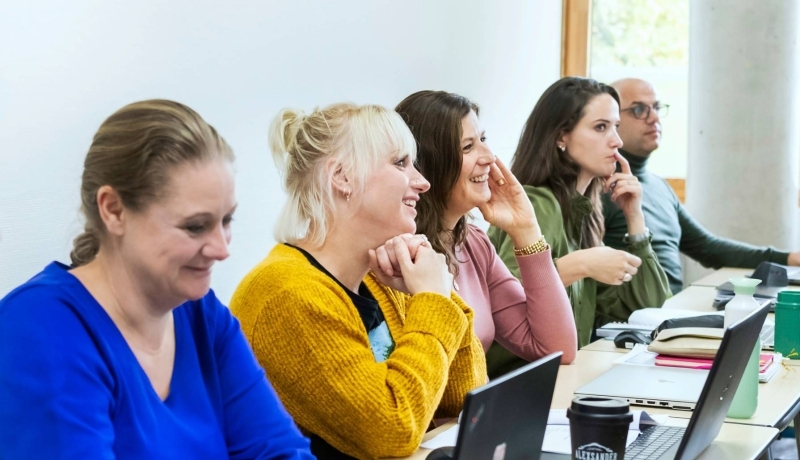 een rij van 5 masterstudenten zitten aan tafel met laptops