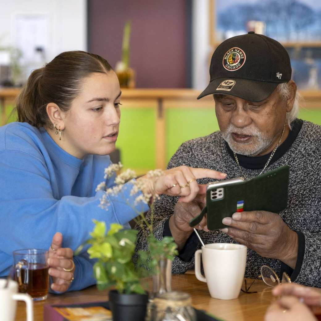 Een oudere man met een Ipad, een jonge dame wijst hem hier iets op aan.