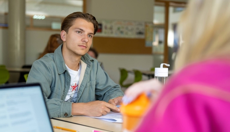 Mannelijke student in de klas luistert naar andere student.