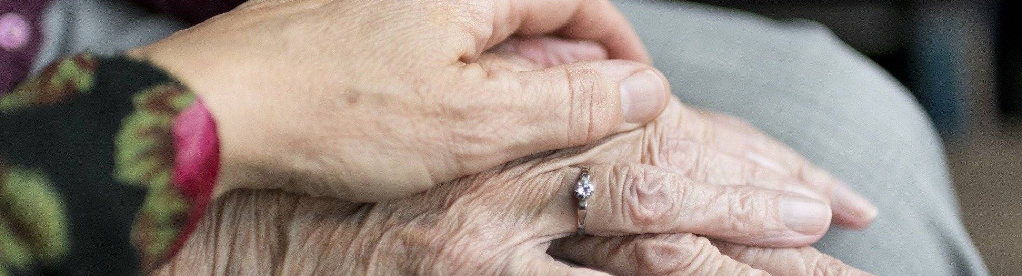 handen oudere en verzorger in beeld