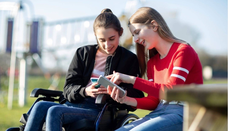 Tiener meisje in rolstoel kijkt naar mobiel met vriendin