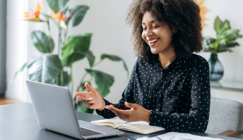 Vrouw zit aan een bureau achter haar laptop. Ze heeft een online vergadering.