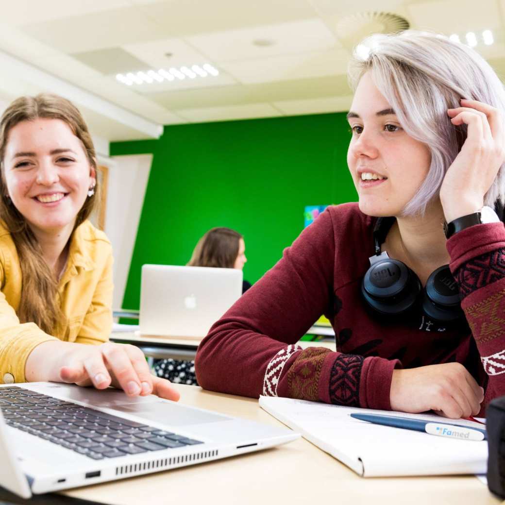 Deelnemers kijken lachend naar de laptop tijdens de ICT-workshop