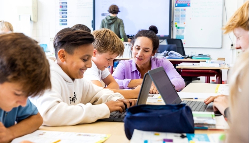 docent kijkt aan tafel bij werkende kinderen